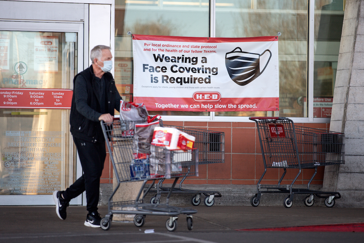 A customer leaves a grocery store in Austin, Texas, wearing a mask and pushing a grocery cart