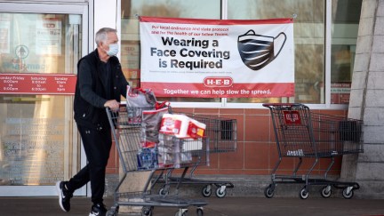 A customer leaves a grocery store in Austin, Texas, wearing a mask and pushing a grocery cart