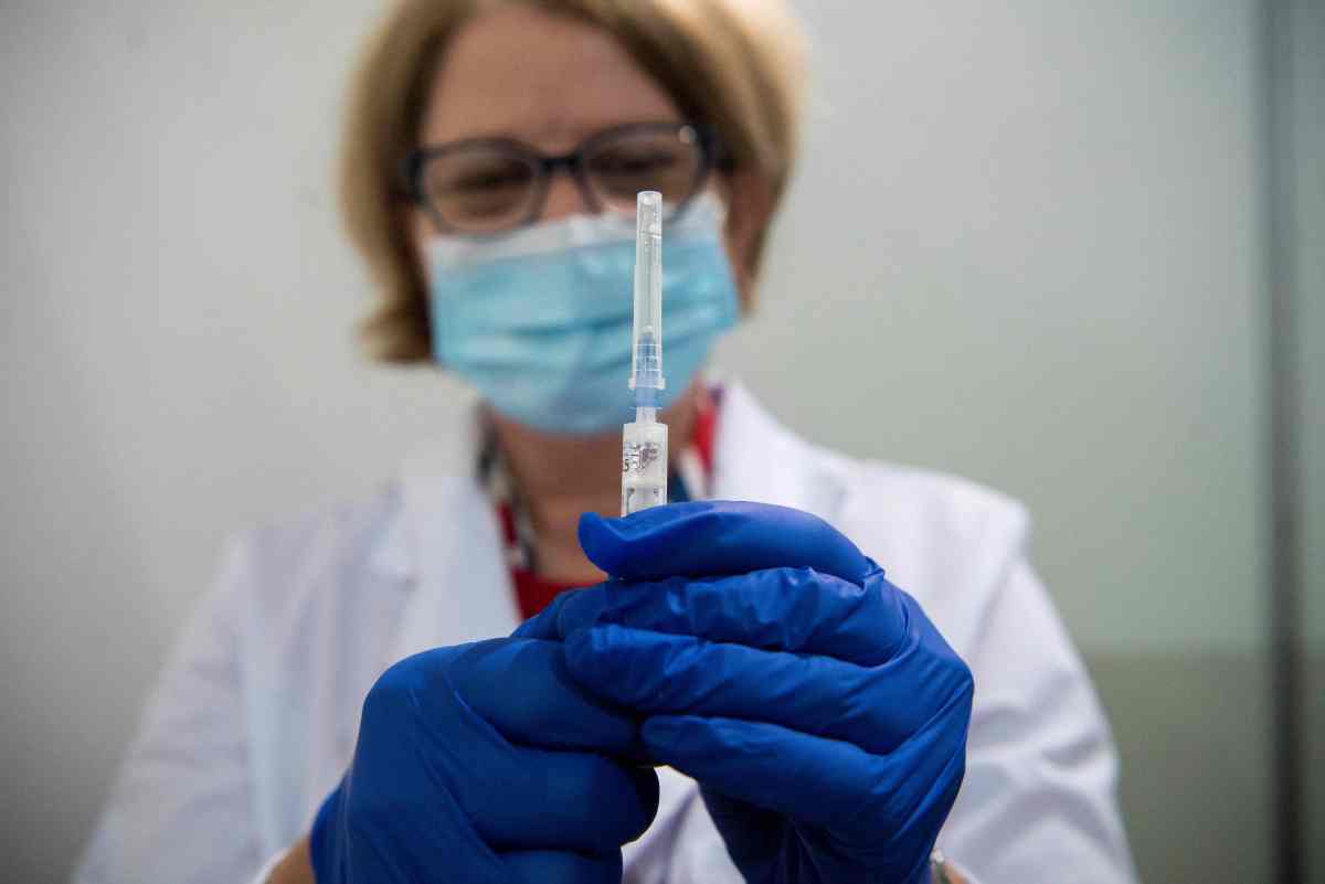 Woman in a mask holding up a syringe.