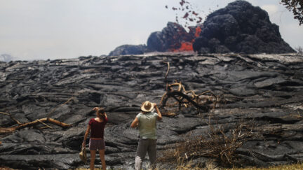 PAHOA, HI - MAY 24: Kate Lilly (L) and Will Divine look on as lava erupts from a Kilauea volcano fissure in Leilani Estates, on Hawaii's Big Island, on May 24, 2018 in Pahoa, Hawaii. An estimated 40-60 cubic feet of lava per second is gushing from volcanic fissures in Leilani Estates. (Photo by Mario Tama/Getty Images)