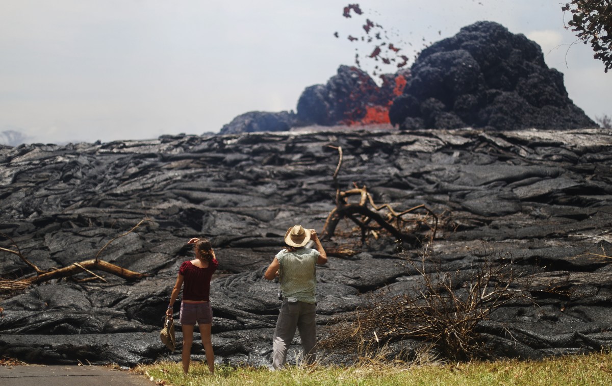 PAHOA, HI - MAY 24: Kate Lilly (L) and Will Divine look on as lava erupts from a Kilauea volcano fissure in Leilani Estates, on Hawaii's Big Island, on May 24, 2018 in Pahoa, Hawaii. An estimated 40-60 cubic feet of lava per second is gushing from volcanic fissures in Leilani Estates. (Photo by Mario Tama/Getty Images)