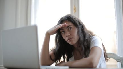 A woman looking annoyed and somewhat confused while sitting at a table with an open laptop