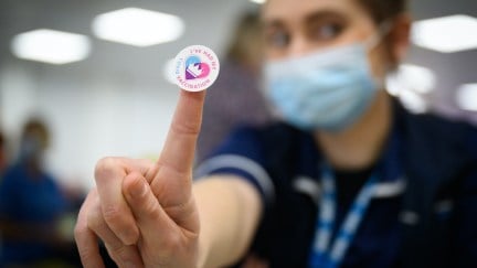 A person in medical gear holds up a sticker reading 