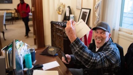Richard Barnett, a supporter of US President Donald Trump, holds a piece of mail as he sits inside the office of US Speaker of the House Nancy Pelosi after protestors breached the US Capitol