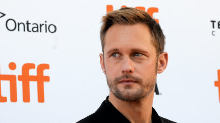 Alexander Skarsgård looks to the side in front of a wall featuring the TIFF logo.
