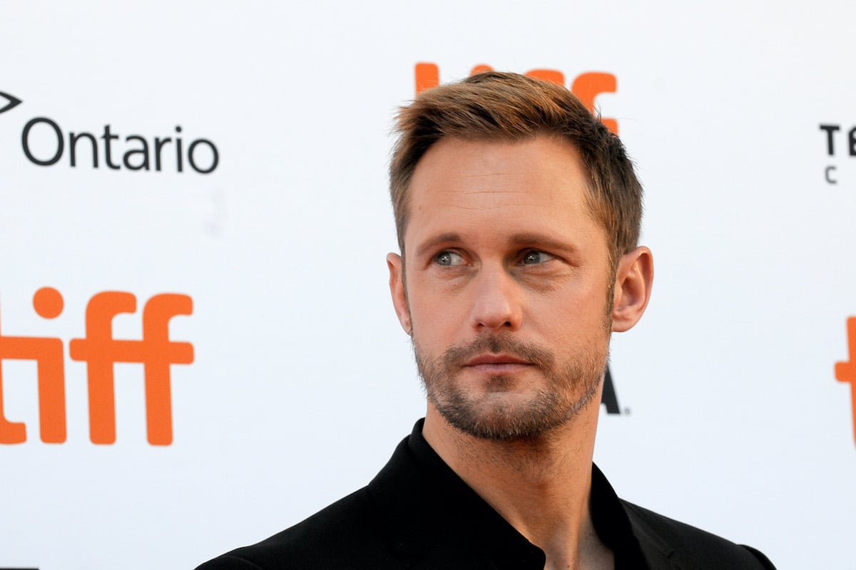 Alexander Skarsgård looks to the side in front of a wall featuring the TIFF logo.