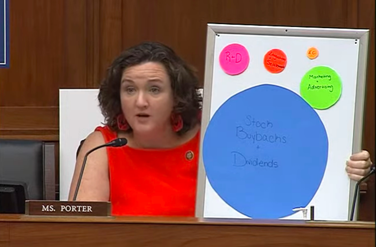 Katie Porter holds a whiteboard with cardboard paper circles of various sizes stuck to it during a hearing.