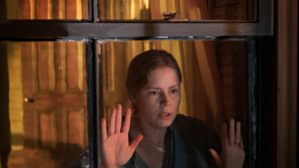 Amy Adams stares out a window with her hands on the glass, looking distressed as Anna Fox in Woman in the Window (2021)