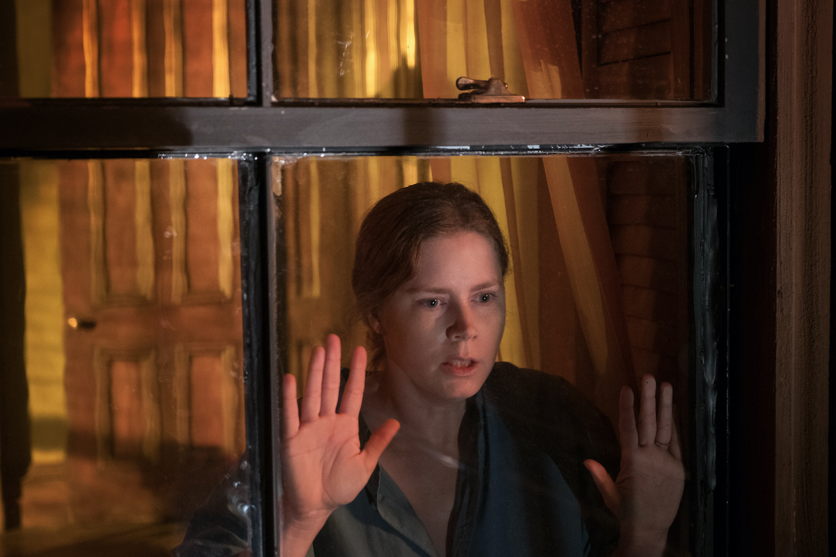 Amy Adams stares out a window with her hands on the glass, looking distressed as Anna Fox in Woman in the Window (2021)