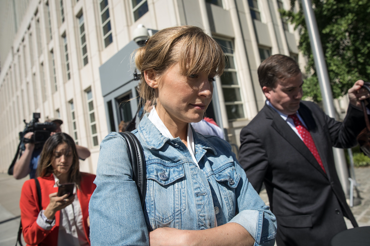 Allison Mack exits court with her arms folded, looking down, wearing a denim jacket.