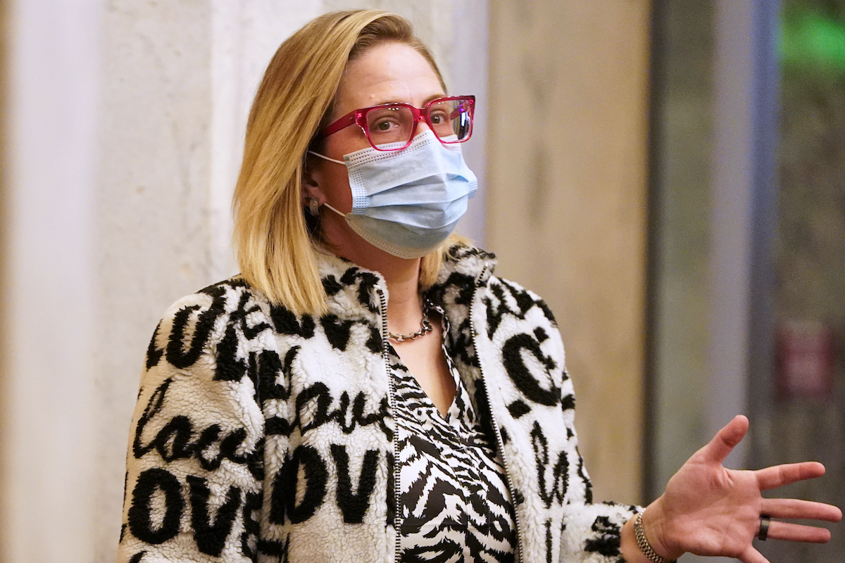 Kyrsten Sinema wears a mask and a coat with the word "love" printed on it