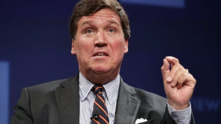 Tucker Carlson talks during a panel, gesturing with his hand.