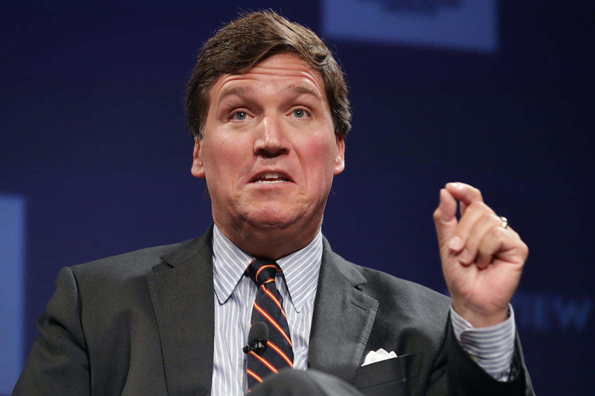 Tucker Carlson talks during a panel, gesturing with his hand.