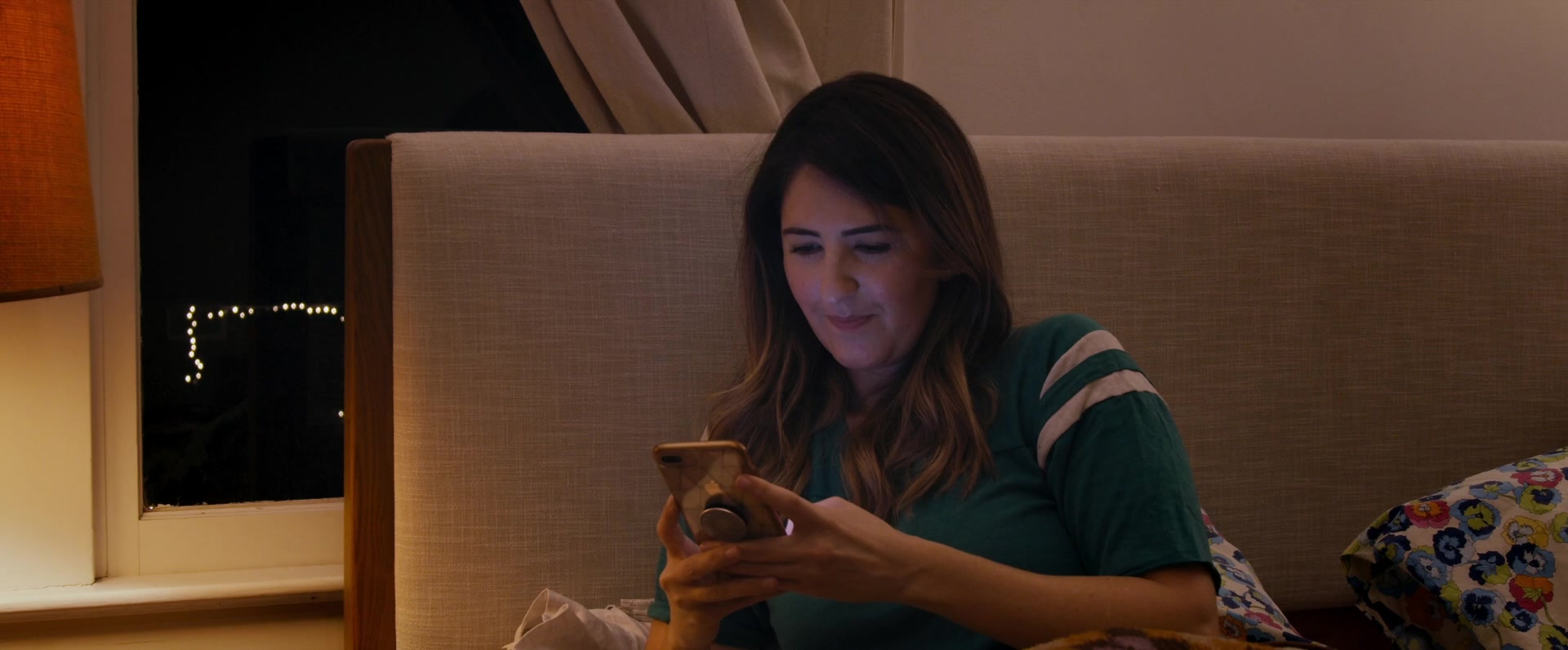 D'Arcy Carden sitting in bed, looking at her phone in Ride the Eagle. 