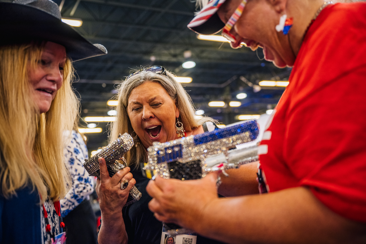 Three women excitedly hold bedazzled handguns at CPAC 2021.