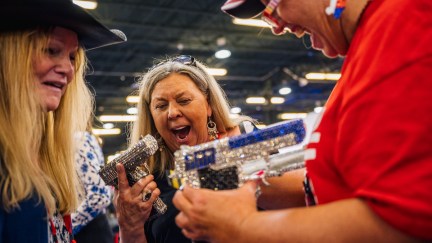 Three women excitedly hold bedazzled handguns at CPAC 2021.
