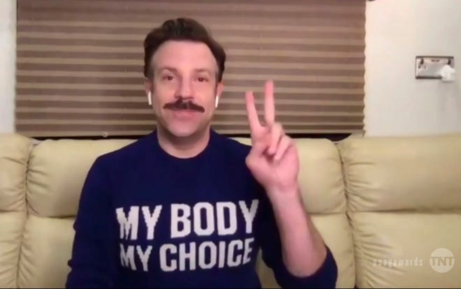 Jason Sudeikis sits on a sofa wearing a My Body, My Choice sweatshirt and gives a peace sign