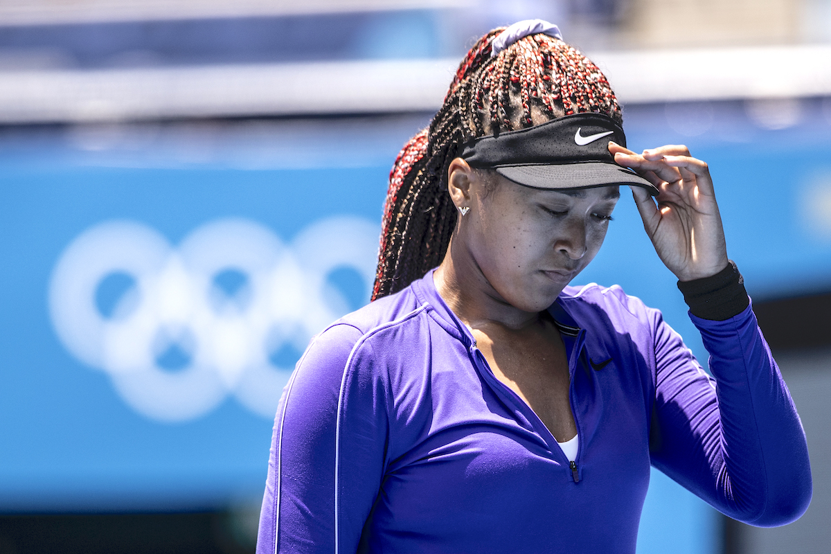 Naomi Osaka adjusts her visor on the tennis court at the Tokyo Olympics