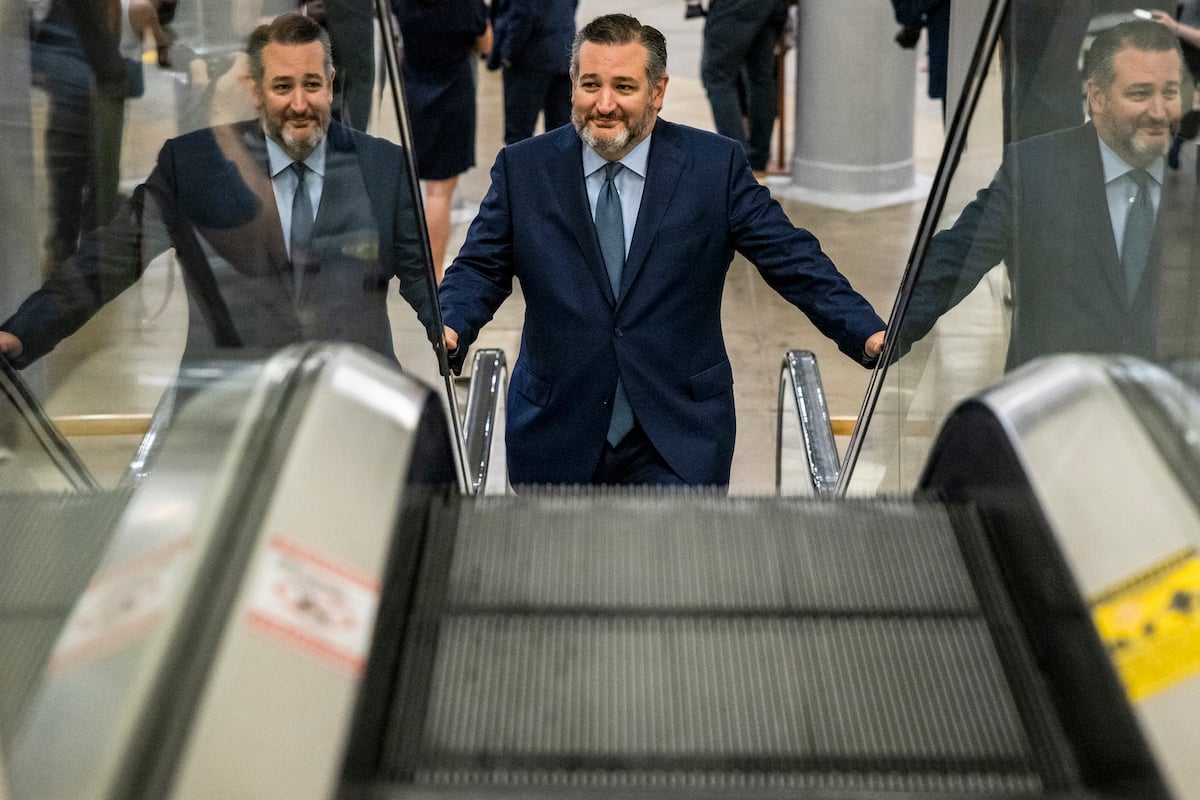 Ted Cruz smiles as he goes up an escalator.