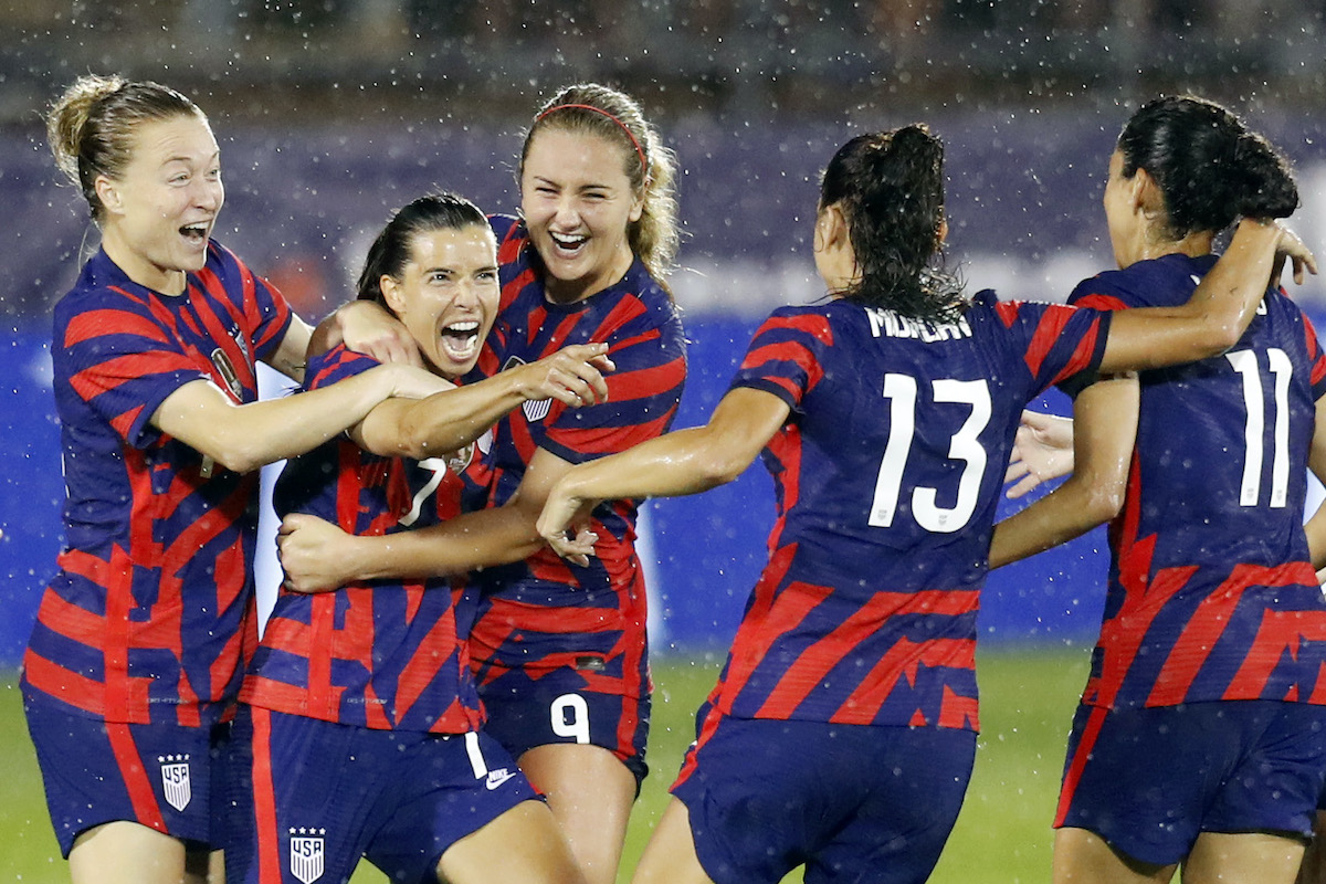 Members of the US Women's national soccer team celebrate and hug after scoring a goal.