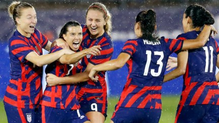 Members of the US Women's national soccer team celebrate and hug after scoring a goal.