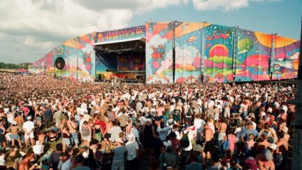A large crowd stands in front of a colorful stage at Woodstock 99.