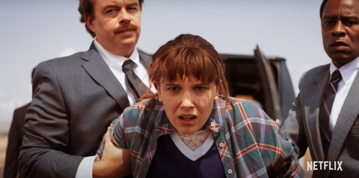 Millie Bobby Brown as Eleven in Stranger Things, being restrained by two men.