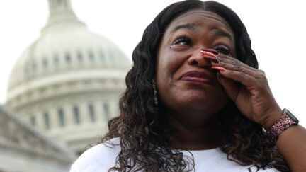 Cori Bush wipes away a tear and smiles with the Capitol building in the backgroud