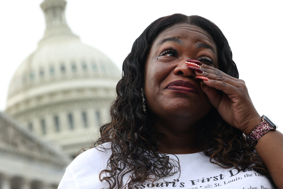 Cori Bush wipes away a tear and smiles with the Capitol building in the backgroud