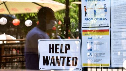 A 'Help Wanted' sign is posted beside Coronavirus safety guidelines in front of a restaurant