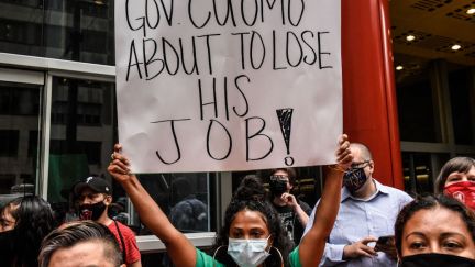 A protester wearing a mask holds a sign reading 