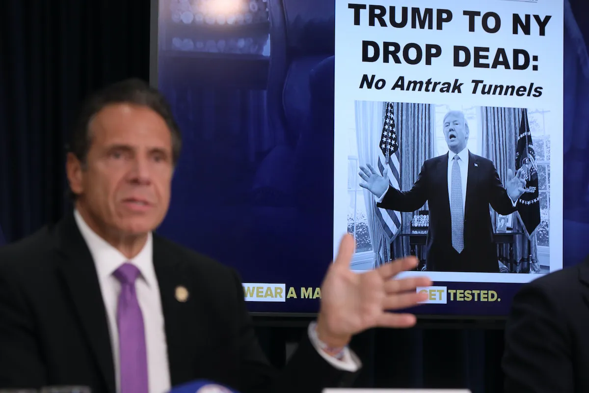 A mock up of a newspaper headline and photo of U.S. President Donald Trump is displayed on a screen as New York state Gov. Andrew Cuomo criticizes Trump's handling of COVID-19 at a news conference