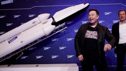 Elon Musk mugs for the camera while posing in front of a model rocket.
