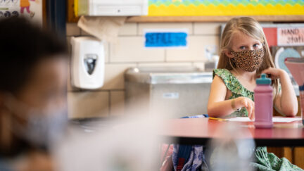 A young student wearing a mask sits and listens in class