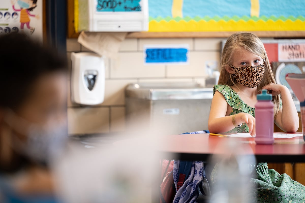 A young student wearing a mask sits and listens in class