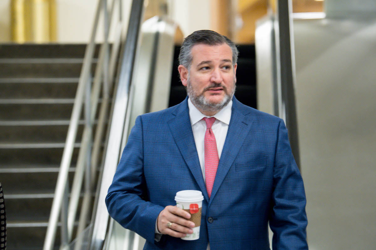 Ted Cruz walks alone through the Capitol holding a cup of coffee.