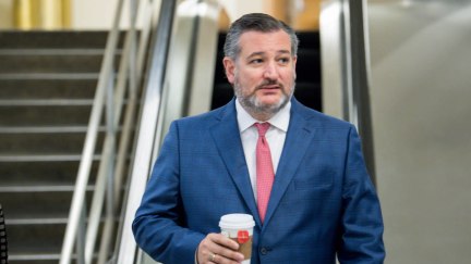 Ted Cruz walks alone through the Capitol holding a cup of coffee.
