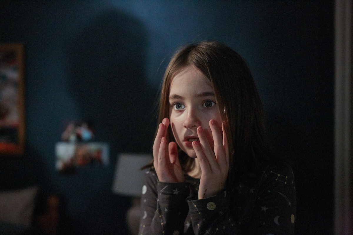 A young girl holds her hands up to her face with a scared expression in a still from Martyrs Lane.