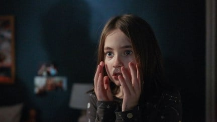 A young girl holds her hands up to her face with a scared expression in a still from Martyrs Lane.