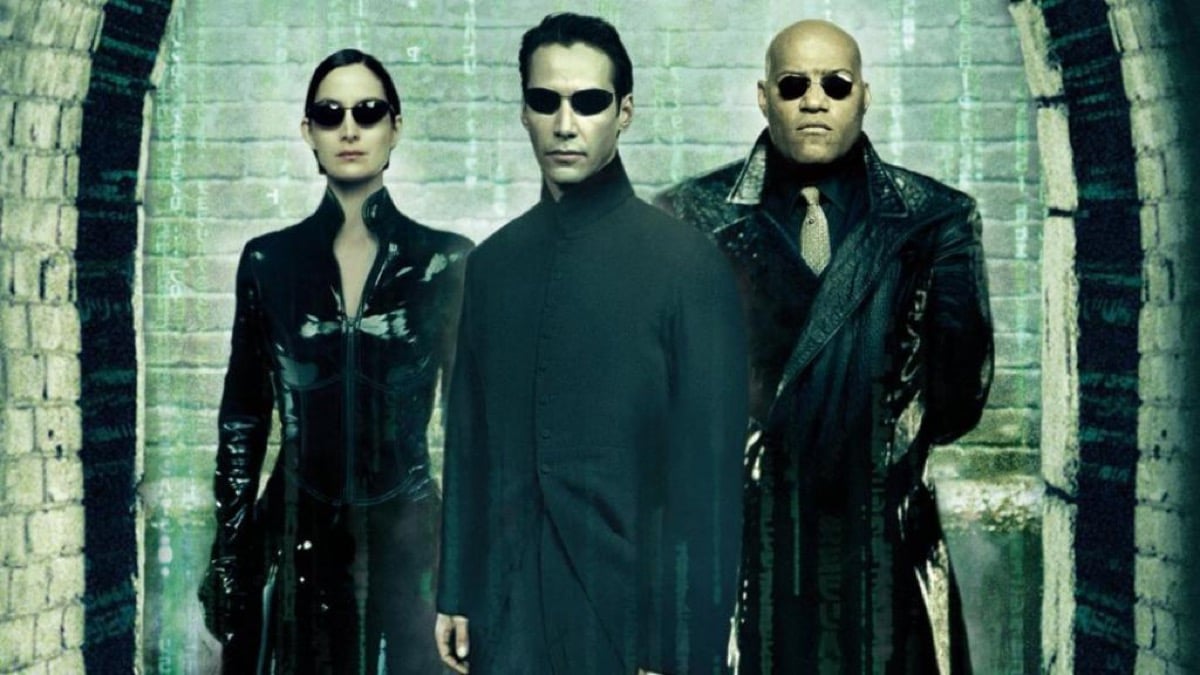 Neo (Keanu Reeves), Trinity (Carrie-Anne Moss), and Morpheus (Laurence Fisburne) standing together and staring into the camera in dark sunglasses in The Matrix Reloaded poster.