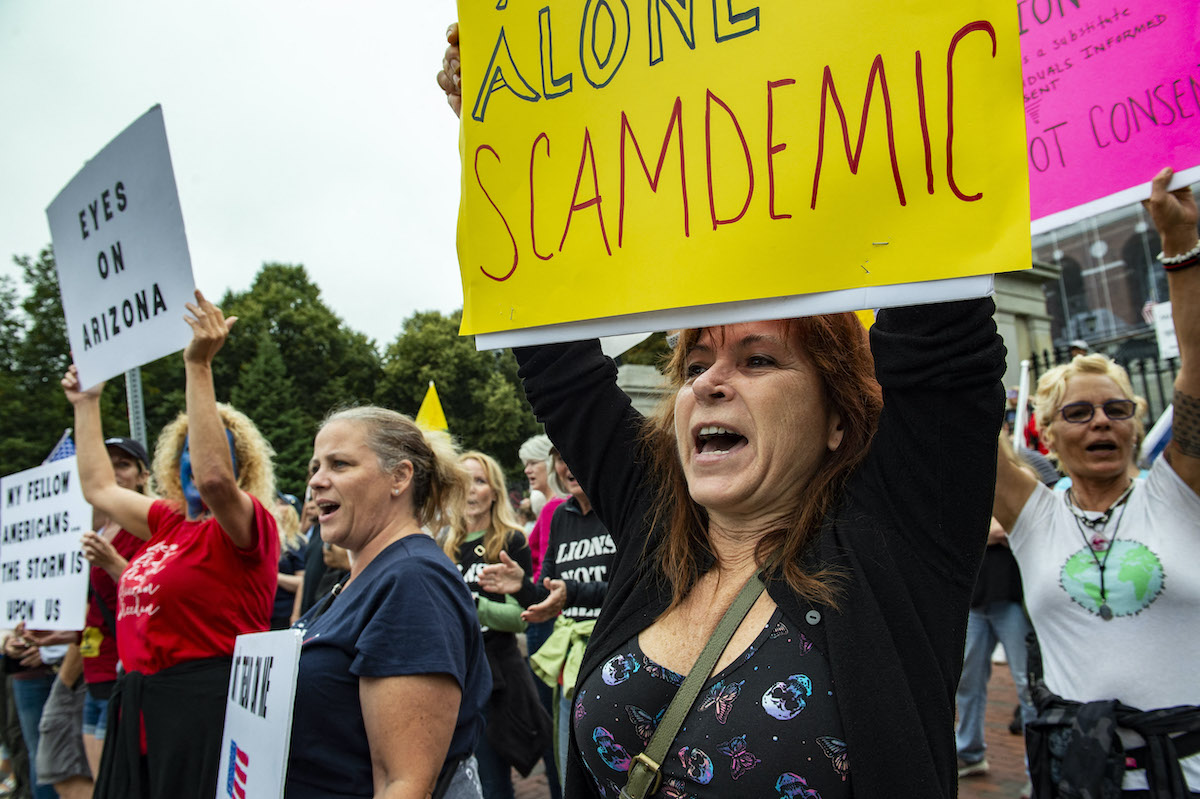 A gathering of anti-vaccine protesters hold signs and yell