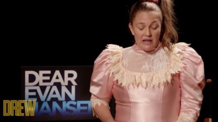 Drew Barrymore in character as Josie Geller from Never Been Kissed, wearing an 80s pink satin prom dress , against a black background with the words Dear Evan Hansen behind her.