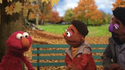 Elmo talking with a Black child and parent at a park. (Image: Sesame Street/HBO.)
