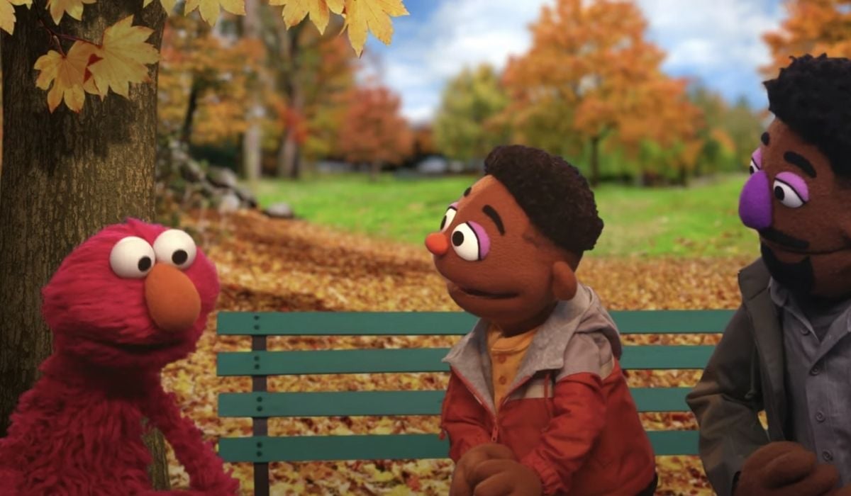 Elmo talking with a Black child and parent at a park. (Image: Sesame Street/HBO.)