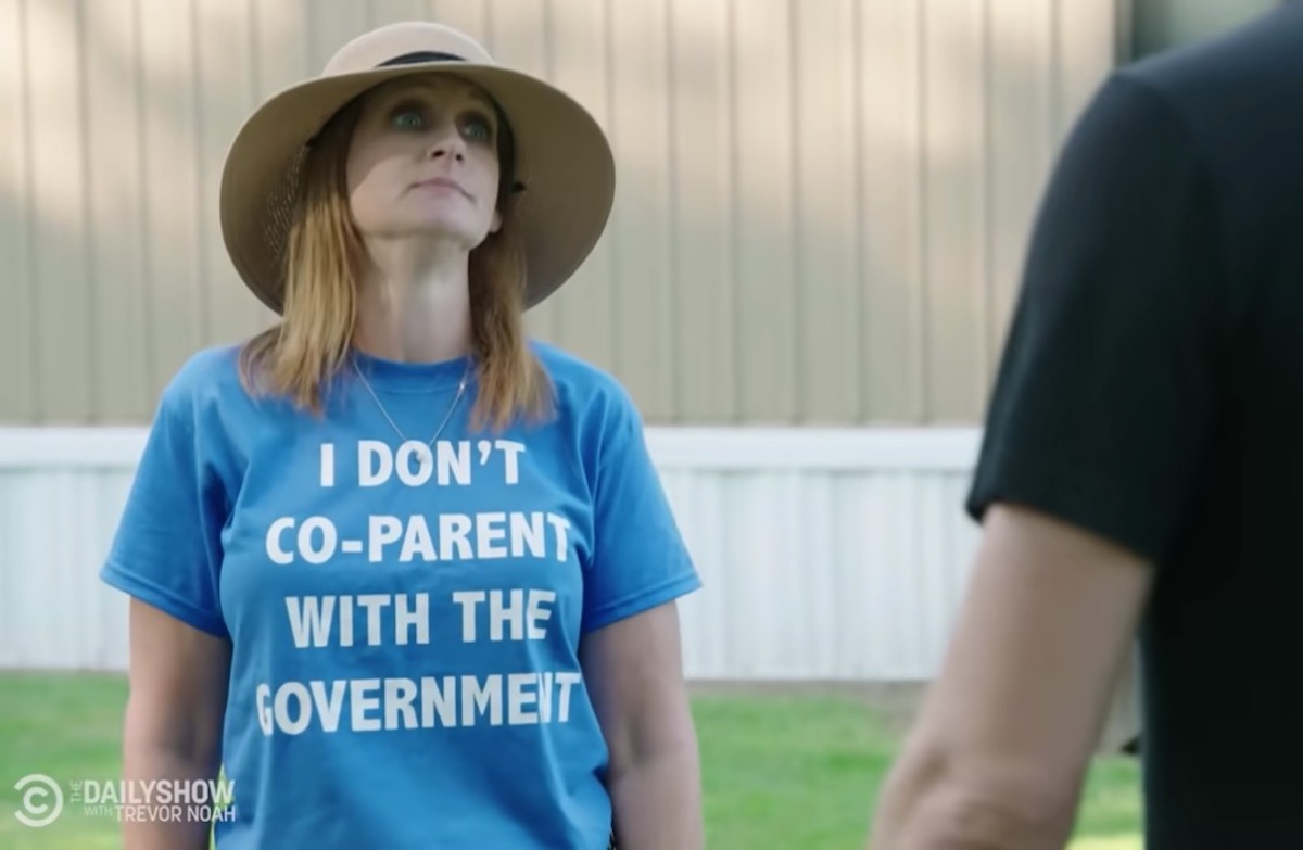 A white woman wearing a sunhat and a blue t-shirt reading "I don't co-parent with the government" talks to a man off-camera