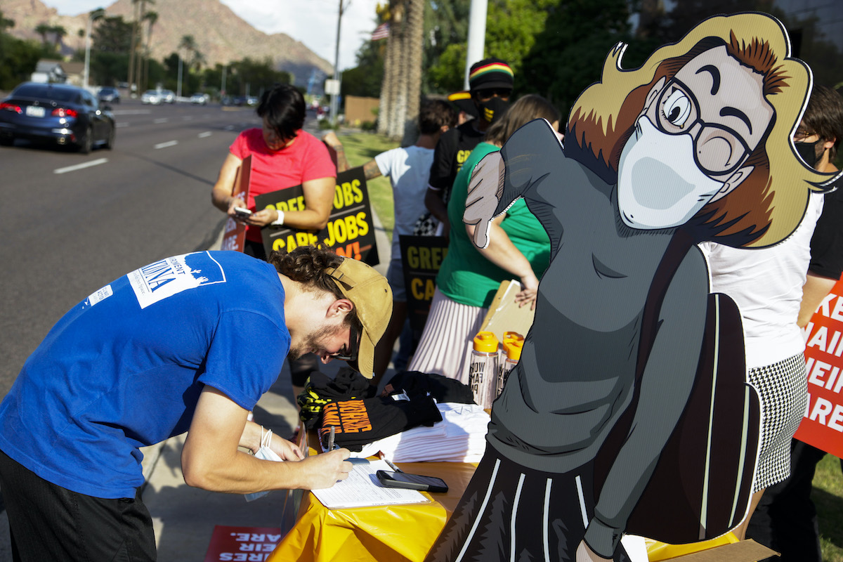 Protesters for green jobs attend a rally featuring a cartoon cutout of Kyrsten Sinema