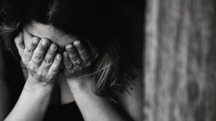 Black and white image of someone crying into their hands. (Image: Kat Jayne on Pexels.)