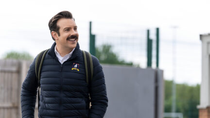 Jason Sudeikis as Ted Lasso, outside, looking to the side, smiling