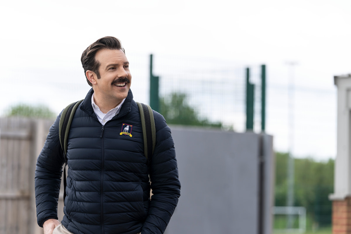 Jason Sudeikis as Ted Lasso, outside, looking to the side, smiling