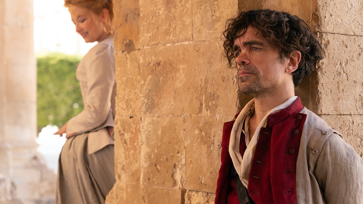 Peter Dinklage and Hayley Bennett standing on opposite sides of the wall in Cyrano